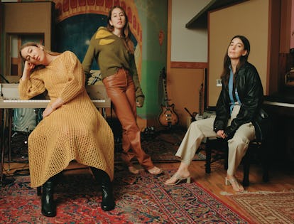 Este Haim in a yellow knit dress, Alana Haim in a green sweater and brown pants, and Danielle Haim i...