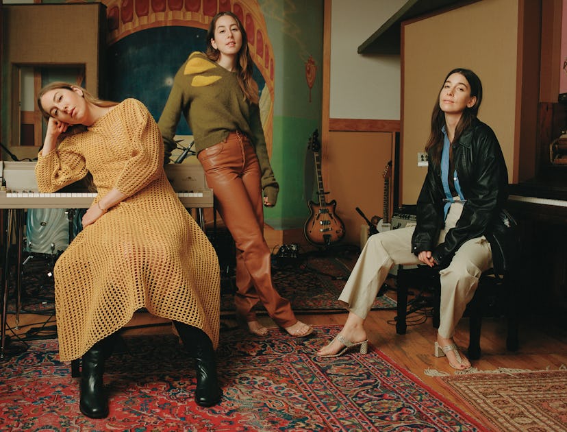 Este Haim in a yellow knit dress, Alana Haim in a green sweater and brown pants, and Danielle Haim i...