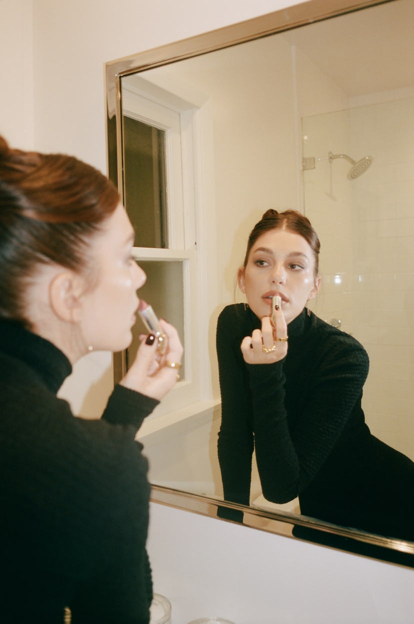 Camilla Morrone applying lipstick in a mirror