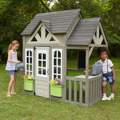 Two kids playing outside in a playhouse made to look like a cottage