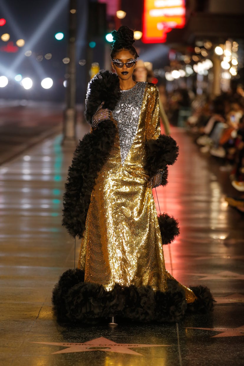Model walks in gold dress and black feather boa at the Gucci Love Parade in Los Angeles