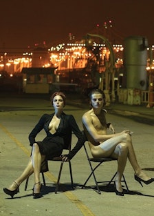two models in folding chairs on a dark street