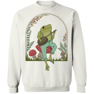 Frog from "Frog and Toad" playing a banjo while sitting on a mushroom on a hoodie.