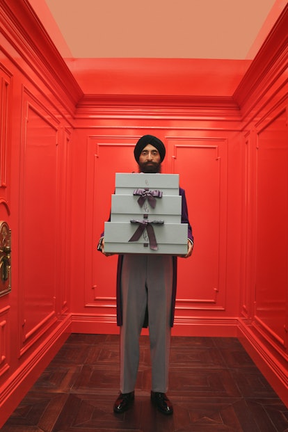 Designer Waris Ahluwalia holding multiple presents in hands while standing in a red elevator