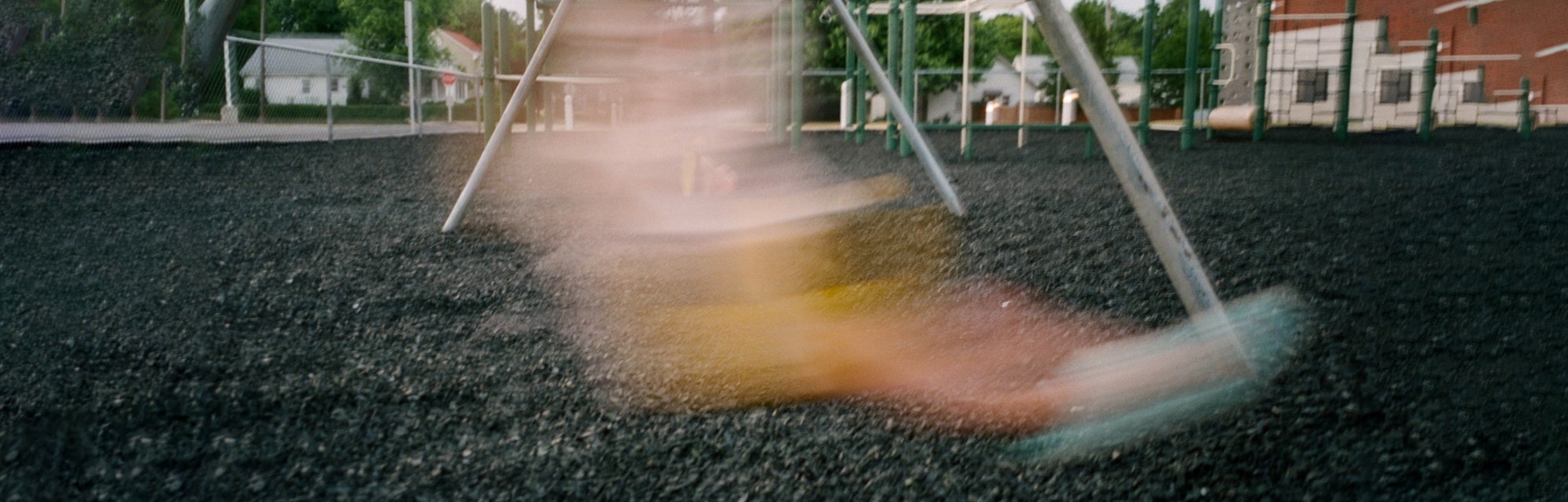 A blurry figure of a child swinging on the swings at a jungle gym
