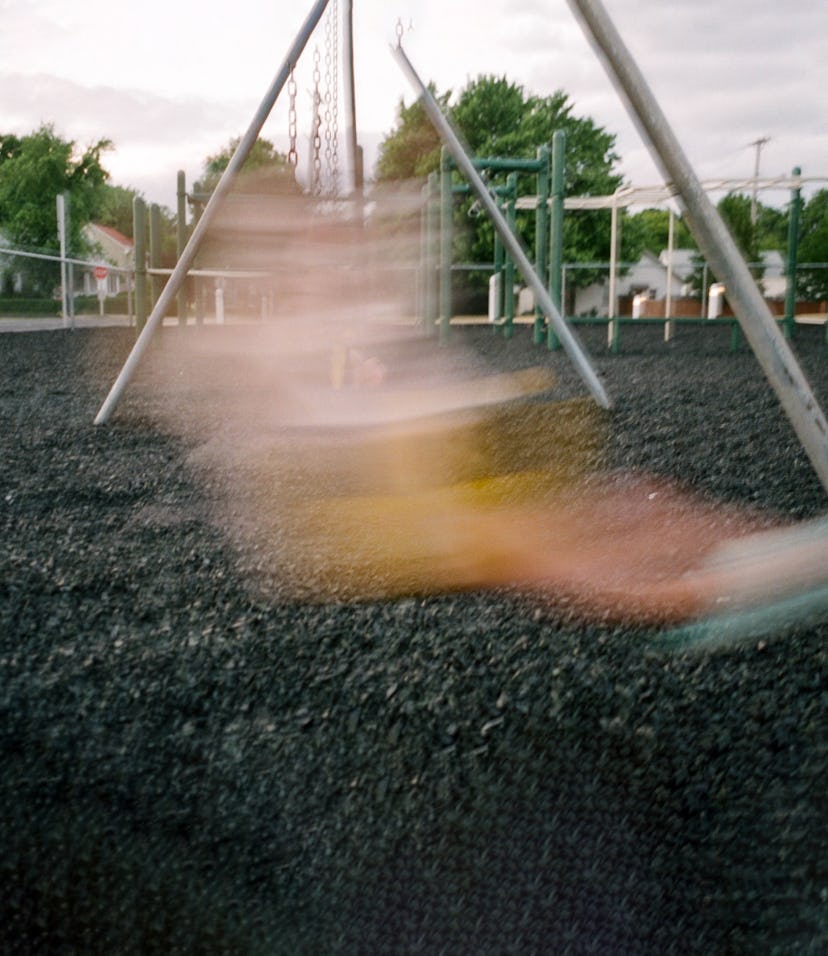 A blurry figure of a child swinging on the swings at a jungle gym