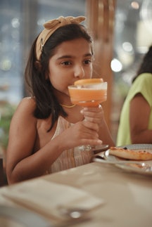 Little girl at a dinner table, sipping a mocktail