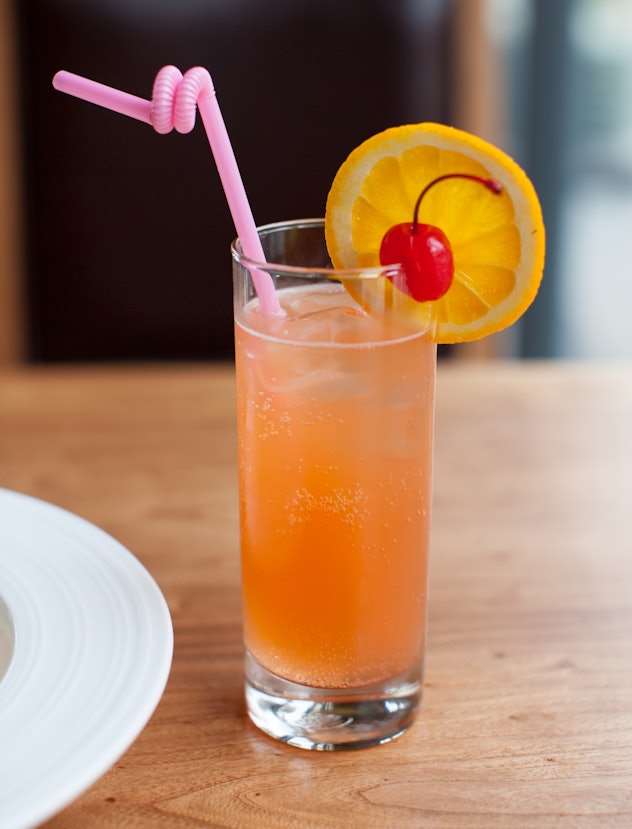 Glass with orange mocktail, twisty straw, and fruit garnish