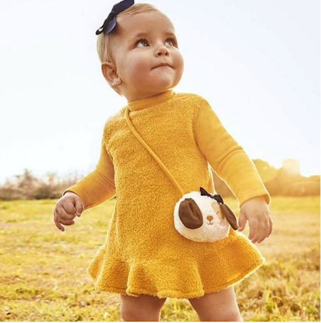 Image of a toddler in a yellow knit dress with decorative purse attached.