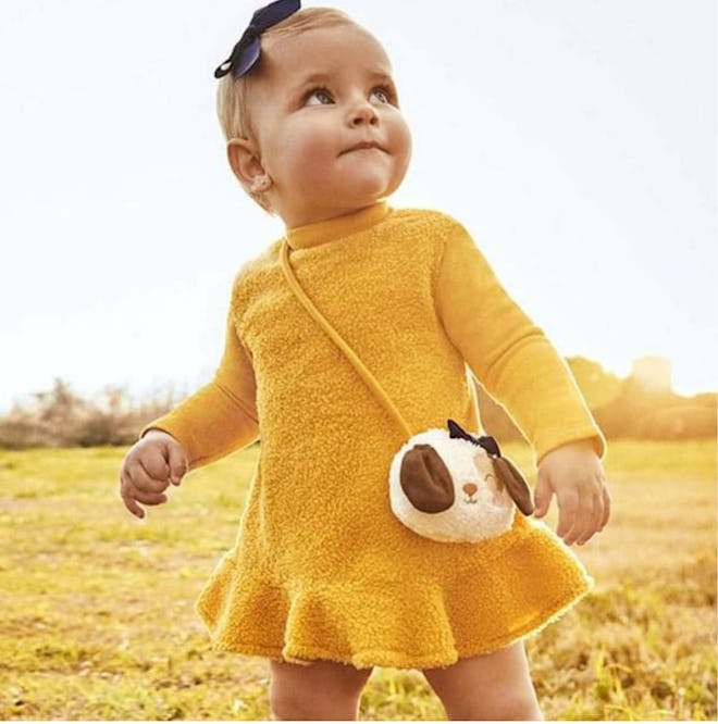 Image of a toddler in a yellow knit dress with decorative purse attached.