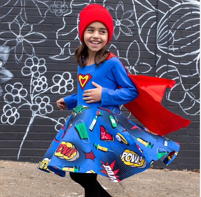Image of a young kid dressed in a blue long-sleeve dress with skirt covered in cartoon-like pictures...