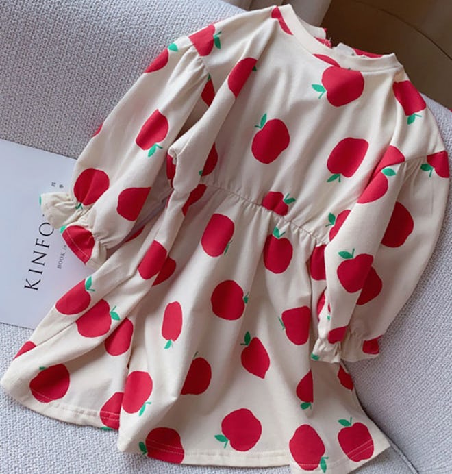 Image of a beige kid's dress with red apple print.