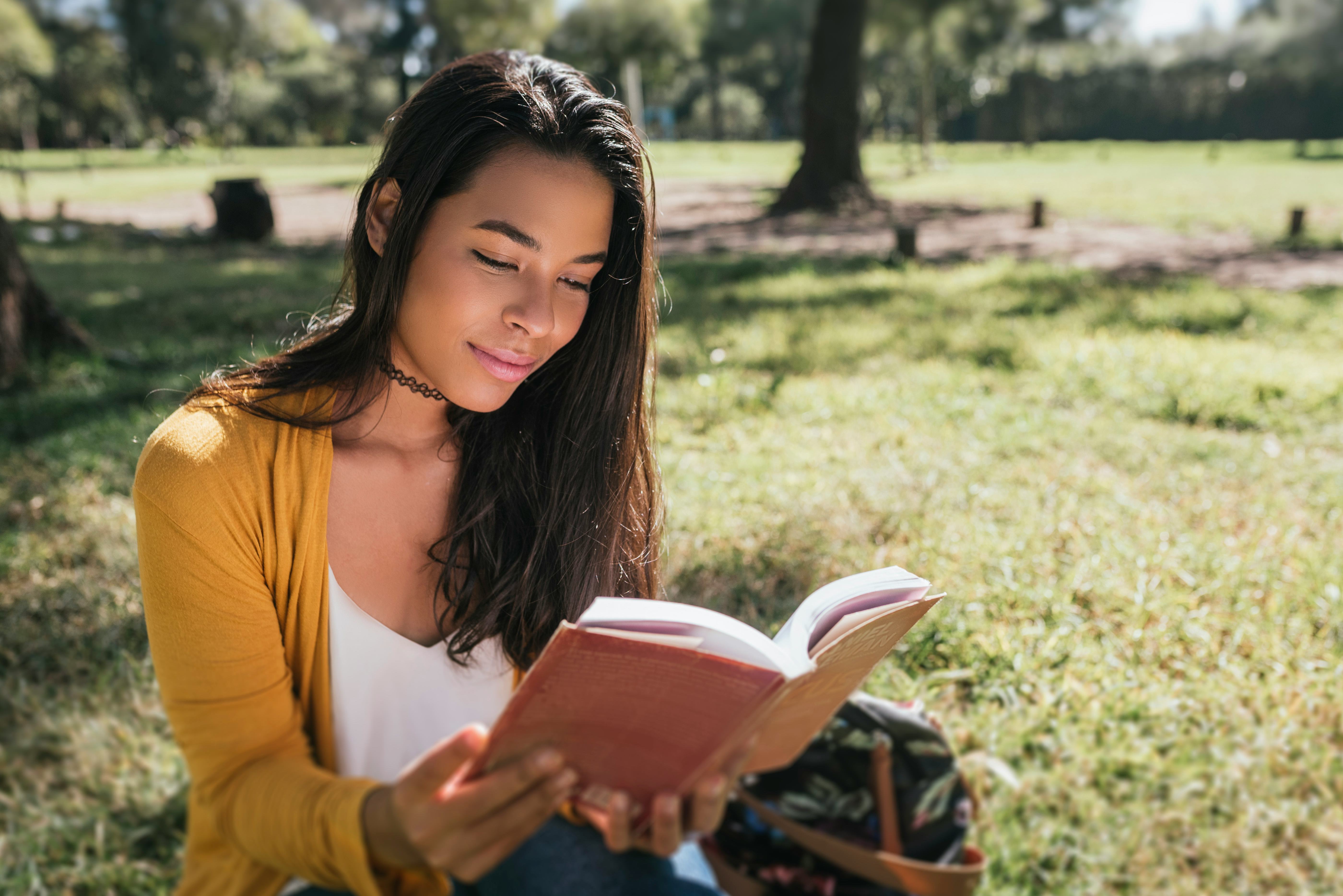Young woman reading book while sitting in a park.
