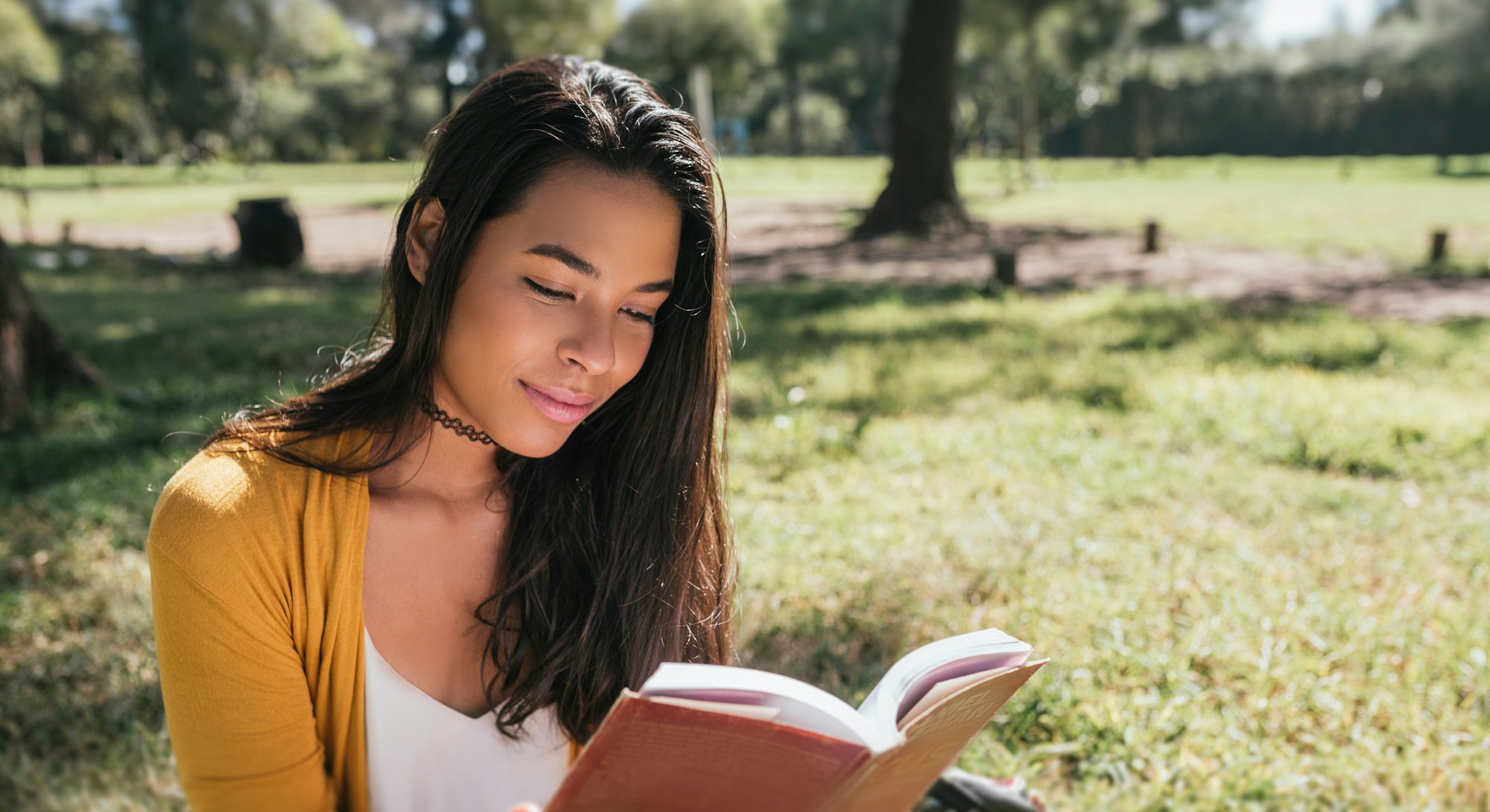 Young woman reading book while sitting in a park.