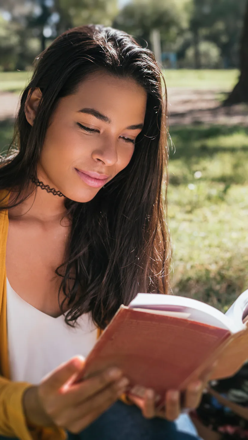 Young woman reading book while sitting in a park.