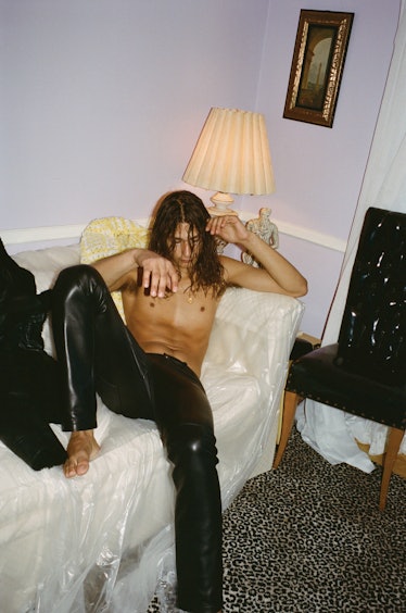 An Altu model lying shirtless and in black leather pants on a white couch