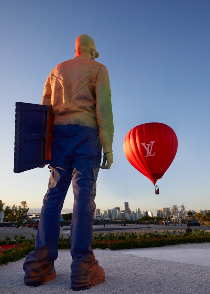 A man standing and looking at a big red Louis Vuitton air balloon in air