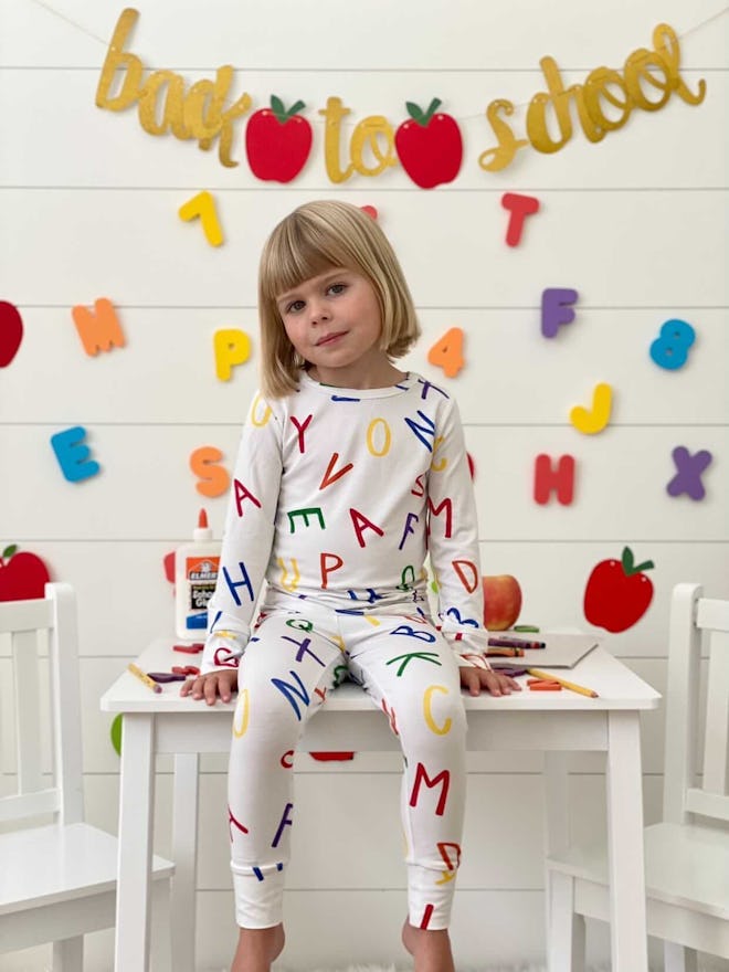Little girl sitting on a desk, modeling long-john pjs with letter print