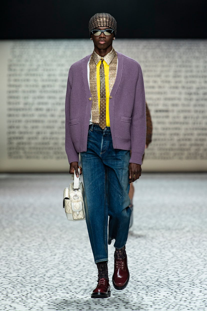 A model walking the Dior Men's Fall 2022 runway in a purple cardigan and jeans 