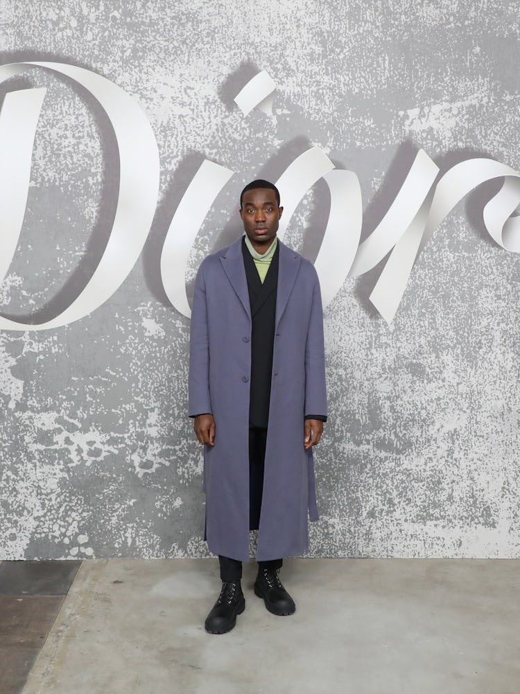 Paapa Essiedu in a violet coat and black suit with a lime turtleneck underneath at Dior Men's Fall 2...