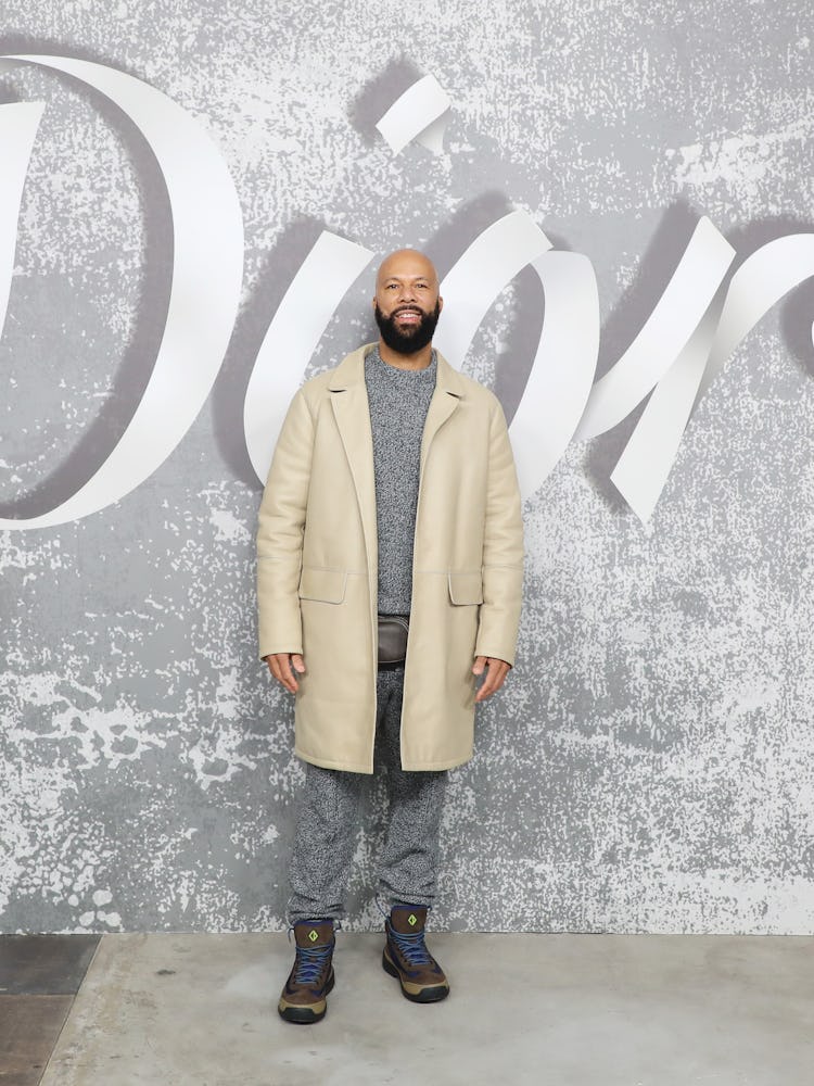 Common wearing a beige coat with a grey set underneath at Dior Men’s Fall 2022