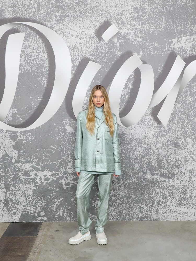 Lila Moss in a light blue suit with a matching turtleneck underneath and white shoes with a Dior bac...