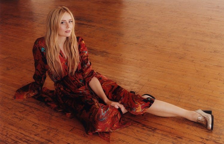 Justine Lupe posing on the floor in a red dress and beige heels 