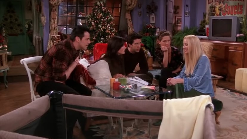 Joey, Monica, Ross, Rachel, and Phoebe gather around a table with a Christmas tree in the background...