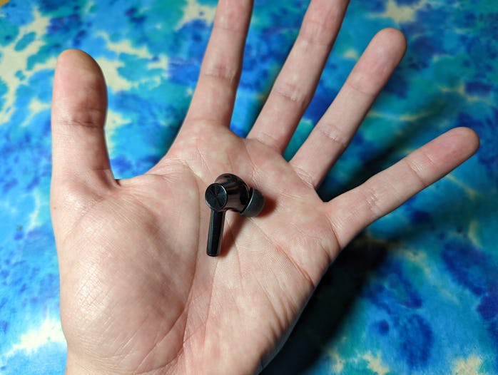 A single OnePlus Buds Z2 earbud on a hand over a blue background.