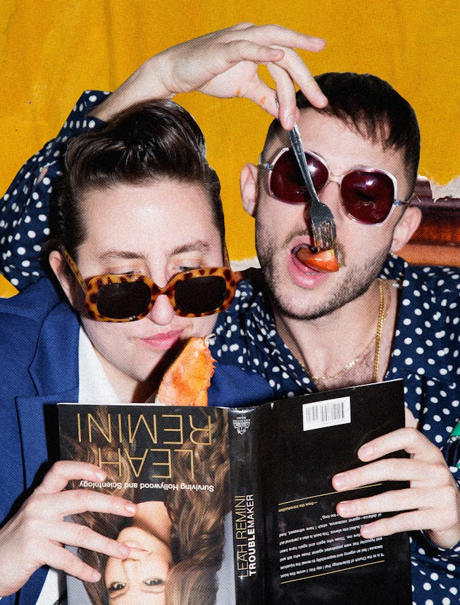 Two people reading Leah Reminis book upside down while wearing sunglasses and eating fruit with a fo...