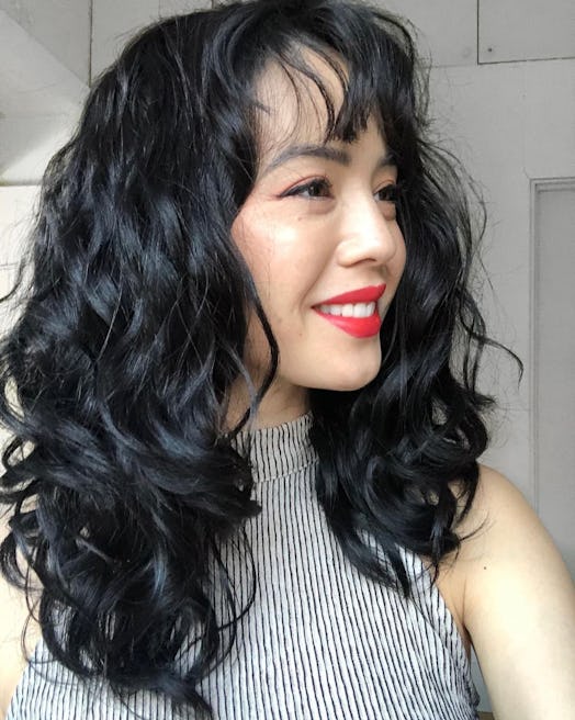 East Asian woman in profile with curly hair and red lipstick
