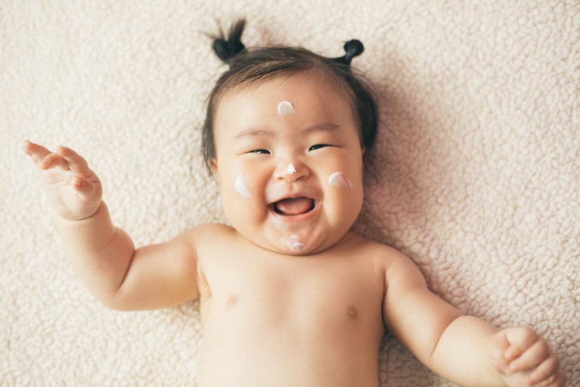 Baby with lotion on her face smiles happily in an article about new year baby names.