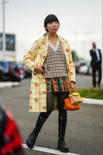 Susanna Lau wears a plaid mini skirt, a sweater vest, and a printed trench coat.