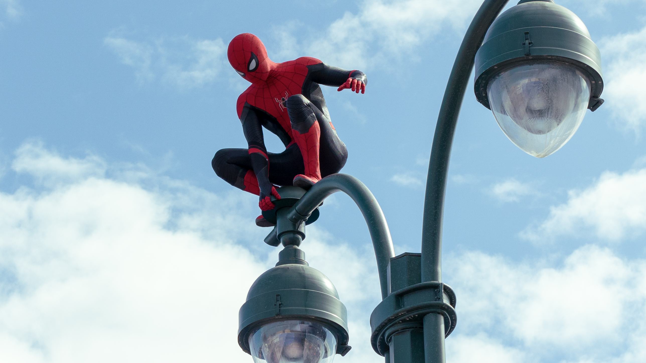 Spiderman looking towards the ground while standing on the streetlight 
