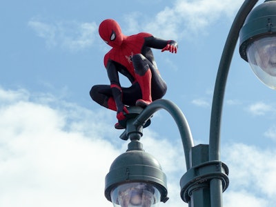 Spiderman looking towards the ground while standing on the streetlight 