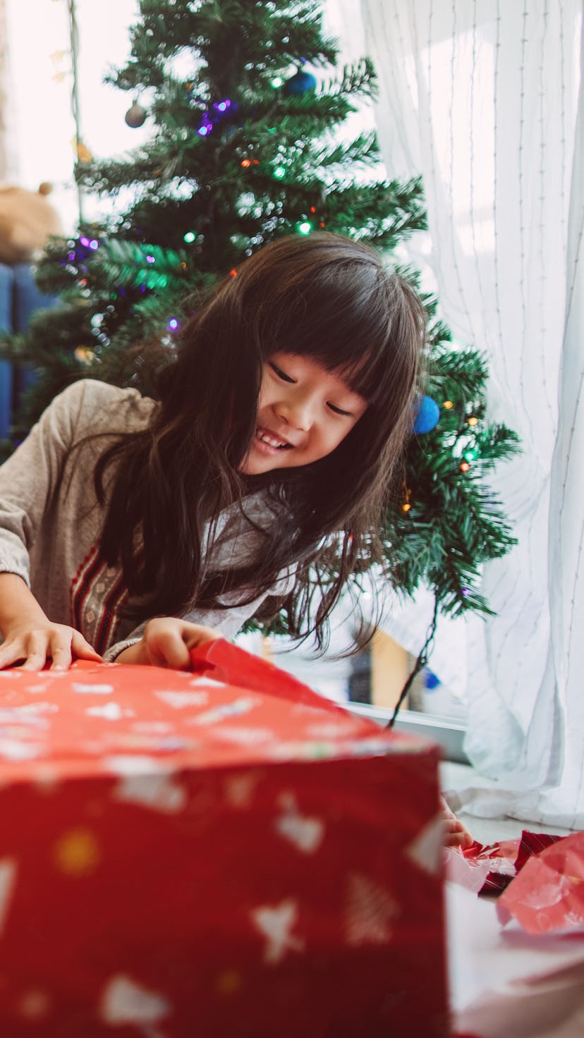 Little girl opening a holiday present in front of a Christmas tree