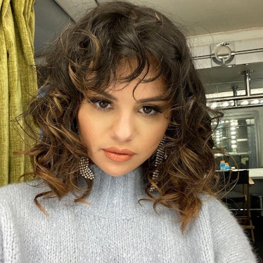 Selena Gomez with a short curly hair, wearing a grey sweater while taking a selfie