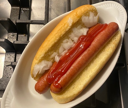Hot dog bun with two hot dogs, onion, and ketchup.