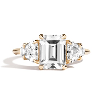 A three-stone engagement ring by Shahla Karimi featuring an emerald cut center stone and triangle si...