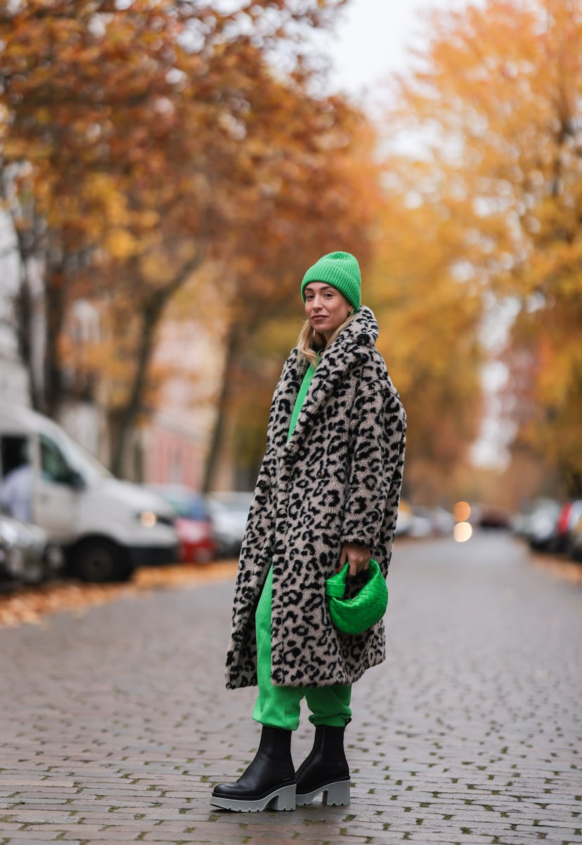 Sonia Lyson wearing a green sweat suit and heat with a cheetah-print coat.