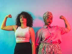 Two young women flexing their muscles after learning their zodiac signs will have the best career ye...