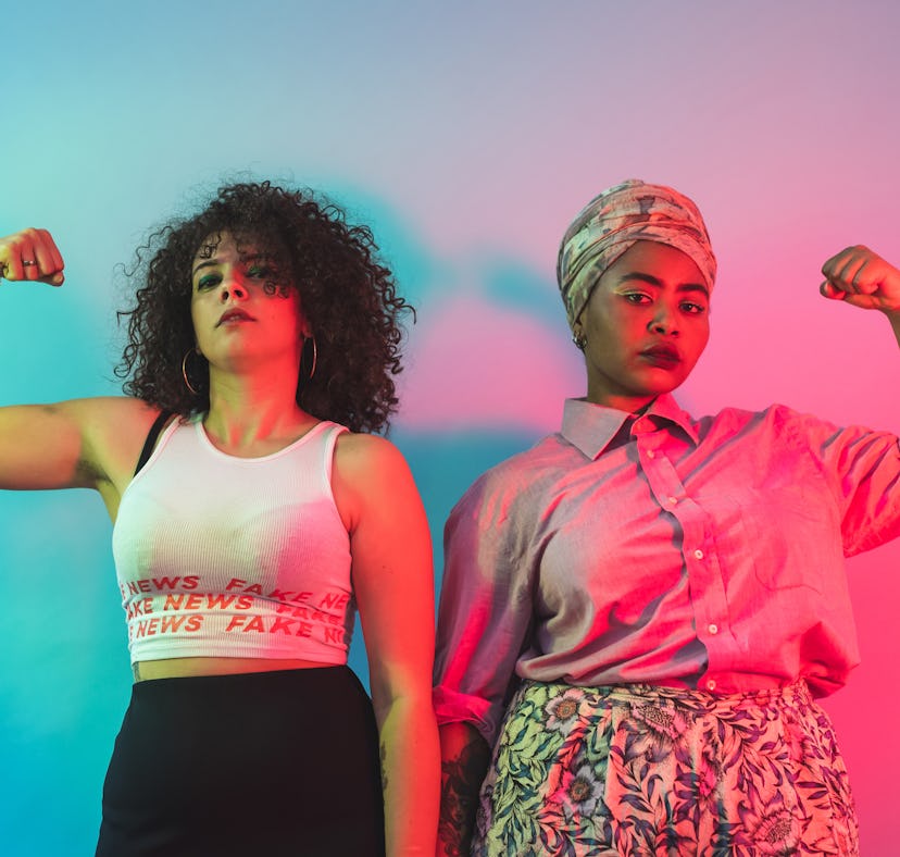 Two young women flexing their muscles after learning their zodiac signs will have the best career ye...