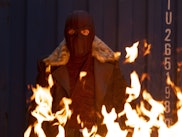 Marvel character wearing a black mask while fire is burning in front of him 