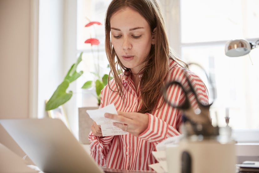 Young woman examining bills while using laptop at home
