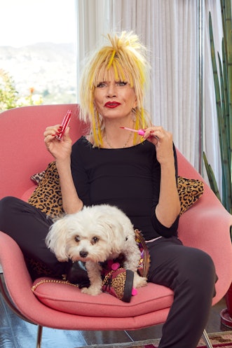 American fashion designer Betsey Johnson sitting in a pink chair with her dog in front of her