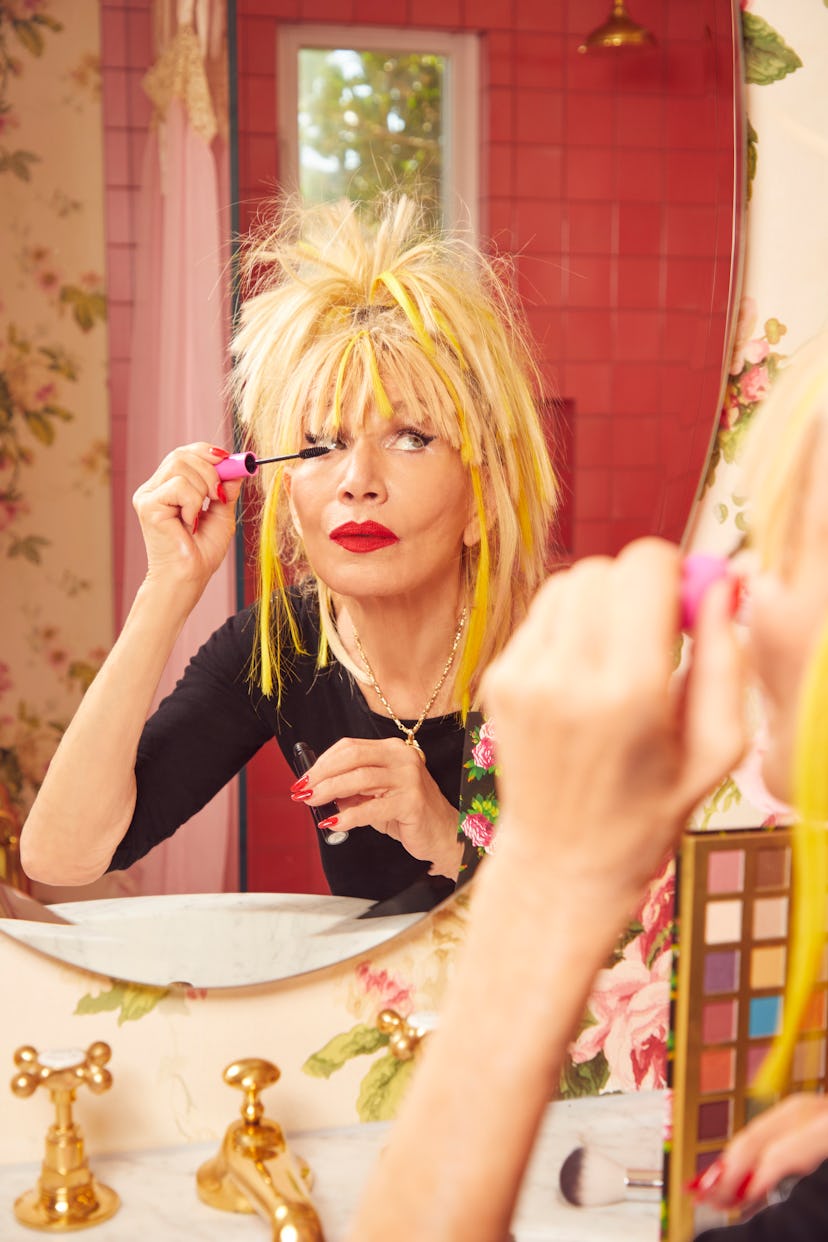 American fashion designer Betsey Johnson standing in front of a mirror in a red-tiled bathroom, doin...