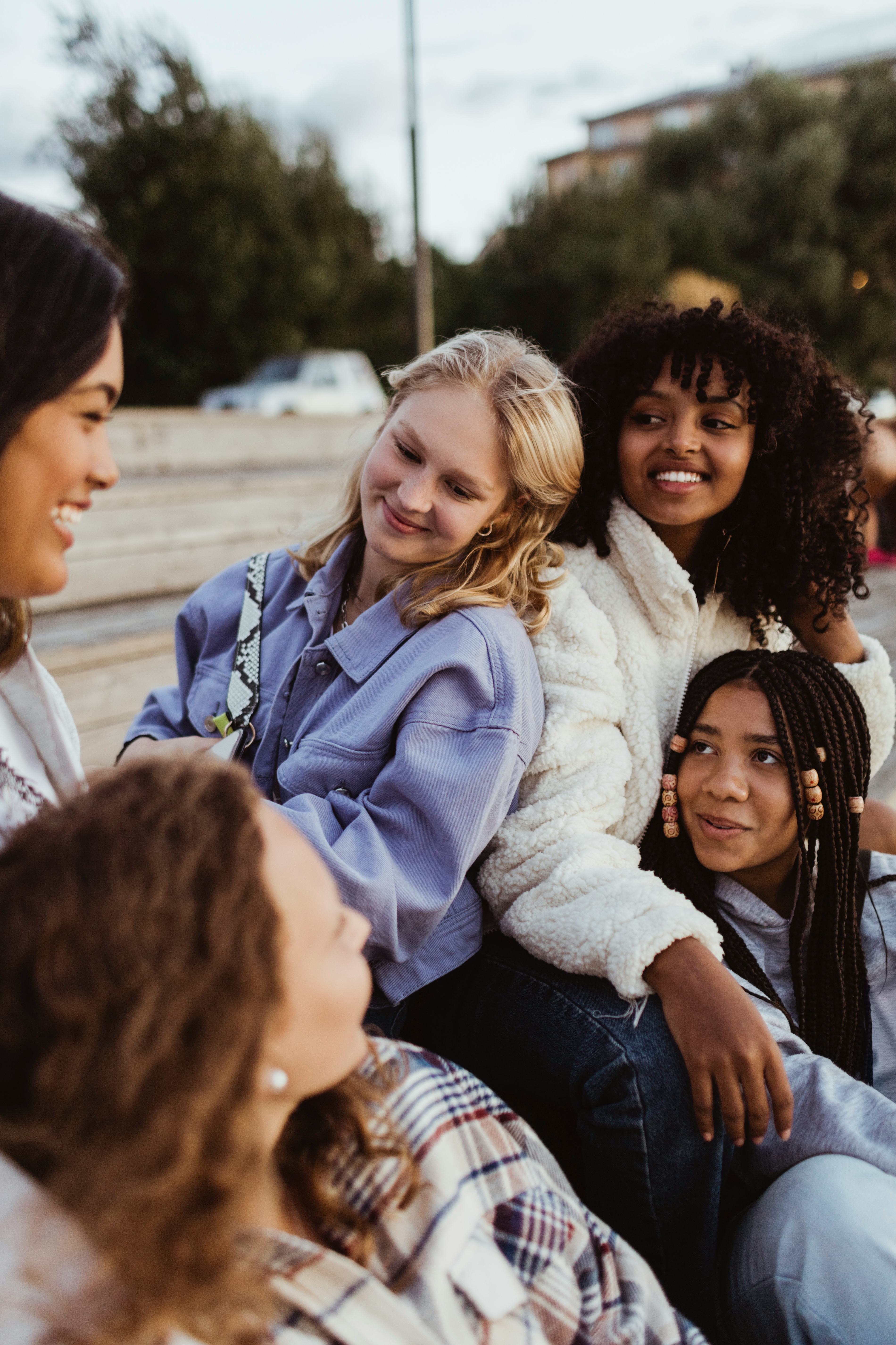 Five young friends smiling at each other outside after learning which zodiac signs will change the m...
