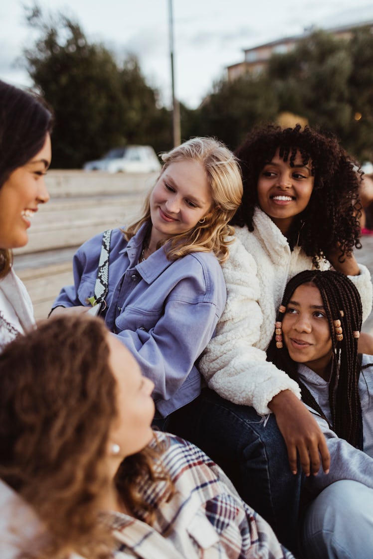 Five young friends smiling at each other outside after learning which zodiac signs will change the m...