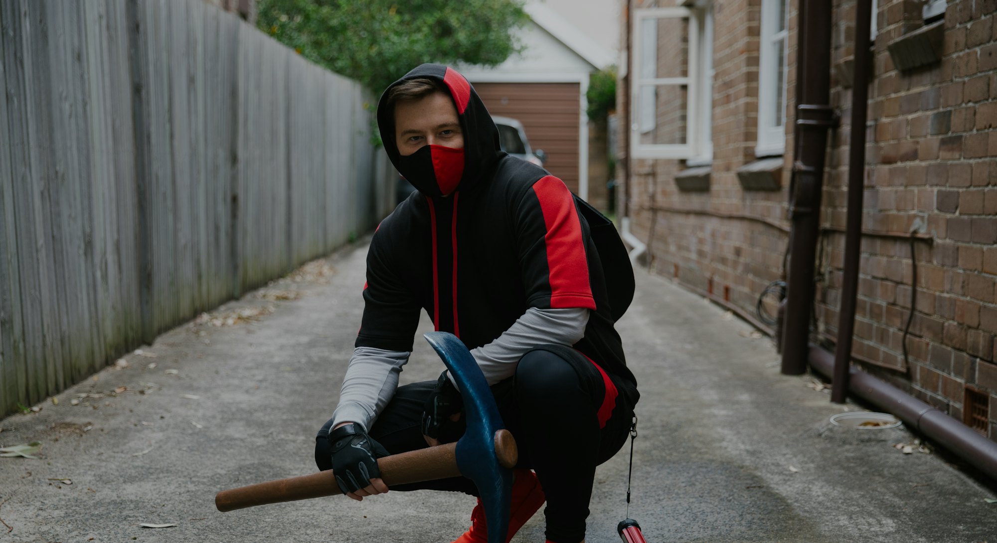 Muselk crouching in red and black ninja-style hoodie and nose/mouth mask while holding a pickaxe.