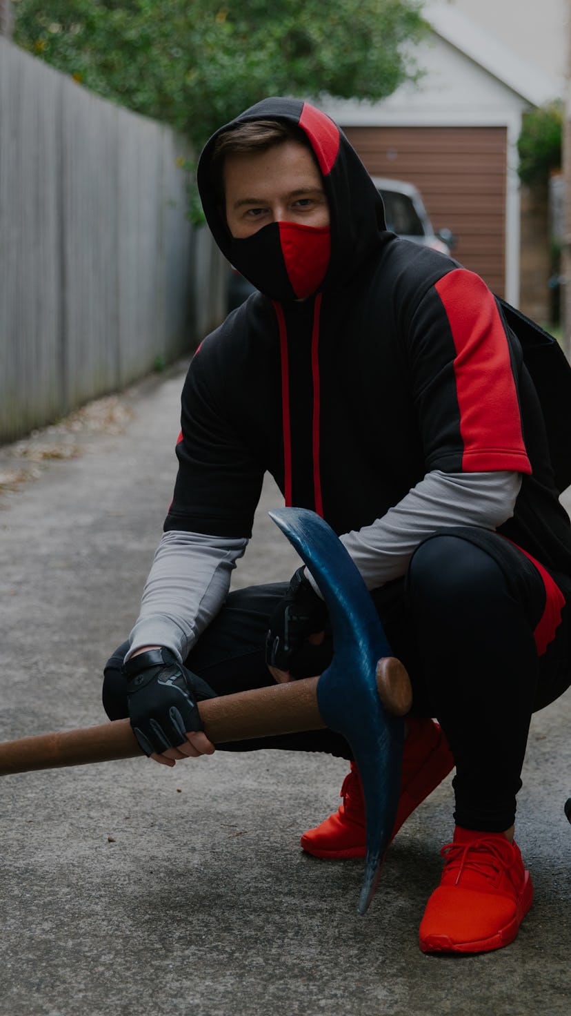 Muselk crouching in red and black ninja-style hoodie and nose/mouth mask while holding a pickaxe.